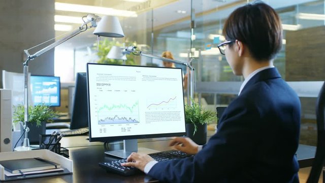 In the Office Businessman Works on the Personal Computer with Spreadsheets, Charts and Statistics. His Colleague sits Opposite to Her. Room is Stylishy made of Concrete and Glass.