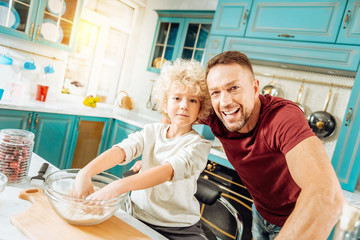 Men in the kitchen. Happy positive loving father smiling and enjoying time with his son while cooking together