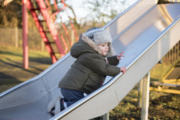 One and a half year old boy playing on a slide in the park
