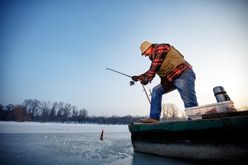 Smiling fisherman catch fish on the frozen river in winter