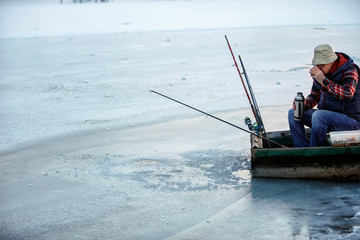 senior man in winter fishing drink tea on frozen lake