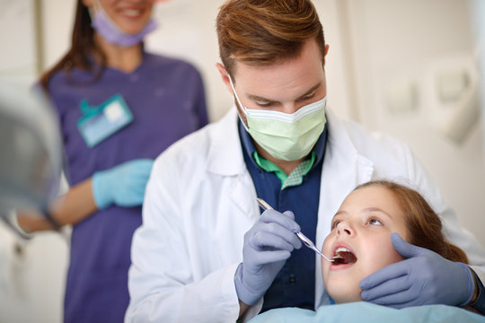 Male dentist looking with dental mirror child's teeth