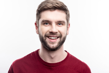 Obraz premium Attractive male. Close up of a handsome upbeat young man in a burgundy t-shirt smiling at the camera while posing isolated on a white background