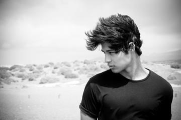 Beautiful young boy on the right of the image with wind on the hait. Moving black hair over a nice face. Desert black and white in background.