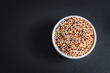 Healthy food  concept Organic raw Quinoa grain mix of 3 colours white, red and black in white ceramic cup on black slate stone plate with copy space 