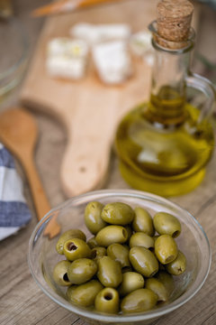 Bowl of green olives and bottle of olive oil over wooden table.