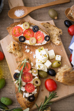 healthy Mediterranean bruschetta on wooden cutting board with vegetables.