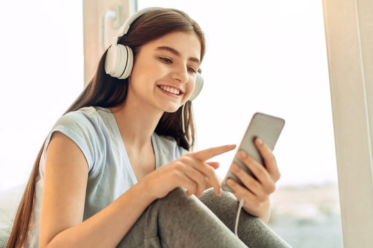 Best music. Beautiful teenage girl scrolling her playlist and choosing the songs to play while listening to the music in the headphones and smiling