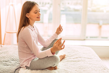 Peaceful inside. The side view of a charming teenage girl sitting cross-legged on the bed and...