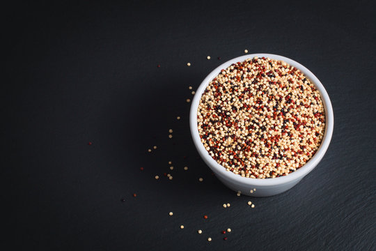 Healthy food  concept Organic raw Quinoa grain mix of 3 colours white, red and black in white ceramic cup on black slate stone plate with copy space 