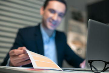 I need this. Selective focus of paper which lying on the table and male hand taking it while laptop standing on the surface