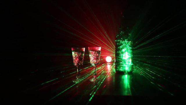 Two glasses of Vodka with bottle on dark foggy club style background with glowing lights (Laser, Stobe) Multi colored. Club drinks theme decoration. Empty space. Selective focus