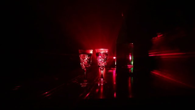 Two glasses of Vodka with bottle on dark foggy club style background with glowing lights (Laser, Stobe) Multi colored. Club drinks theme decoration. Empty space. Selective focus