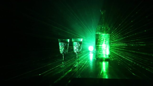 Two glasses of Vodka with bottle on dark foggy club style background with glowing lights (Laser, Stobe) Multi colored. Club drinks theme decoration. Empty space. Selective focus