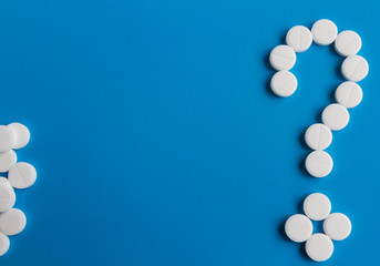 White medical pills question mark on blue background, conceptual image. Medications for the treatment of patients