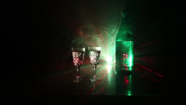 Two glasses of Vodka with bottle on dark foggy club style background with glowing lights (Laser, Stobe) Multi colored. Club drinks theme decoration. Empty space. Selective focus