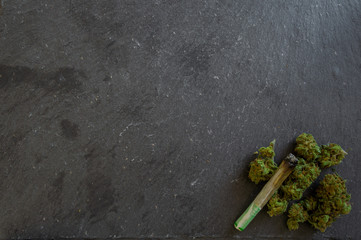 Pile of green marijuana buds and joint lit. Presentation of this natural drug in a black slate...