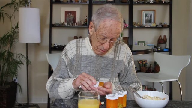 Elderly man takes pill out of pill bottle closes cap