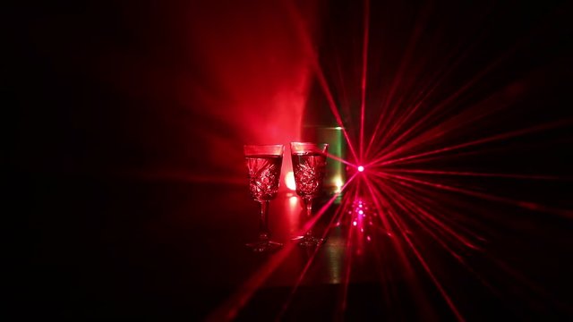 Two glasses of Vodka with bottle on dark foggy club style background with glowing lights (Laser, Stobe) Multi colored. Club drinks theme decoration. Empty space. Selective focus