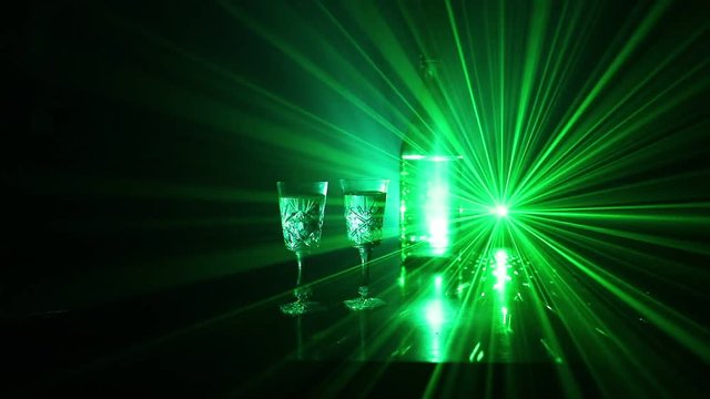 Two glasses of Vodka with bottle on dark foggy club style background with glowing lights (Laser, Stobe) Multi colored. Club drinks theme decoration. Empty space. Selective focus