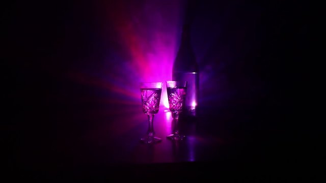 Two glasses of Vodka with bottle on dark foggy club style background with glowing lights (Laser, Stobe) Multi colored. Club drinks theme decoration. Empty space. Selective focus