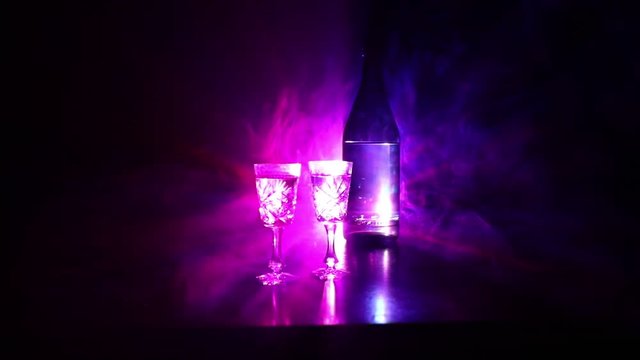 Two glasses of Vodka with bottle on dark foggy club style background with glowing lights (Laser, Stobe) Multi colored. Club drinks theme decoration. Empty space. Selective focus
