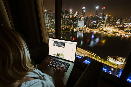  Woman Freelancer Is Working Using Laptop Computer In Home Office At Night. Aerial City Skyline View From Window. Freelance Lifestyle
