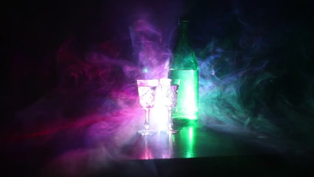 Two glasses of Vodka with bottle on dark foggy club style background with glowing lights (Laser, Stobe) Multi colored. Club drinks theme decoration. Empty space. Selective focus