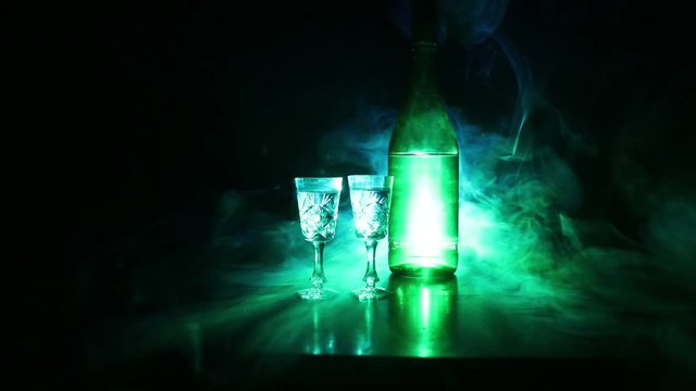 Two glasses of Vodka with bottle on dark foggy club style background with glowing lights (Laser, Stobe) Multi colored. Club drinks theme decoration. Empty space. Selective focus