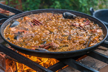 Typical spanish Paella cooked on natural log fire and coal in a traditional fireplace. Seafod, Squid, Mussels, Shrimps, Crabs and green beans
