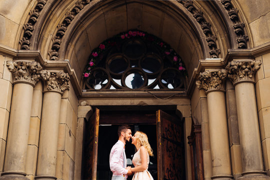 The boyfriend and his girlfriend stand face to face and laugh with arch with columns and wooden doors behind