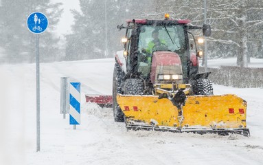 Red tractor with yellow plow removing snow during blizzard. Street maintenance