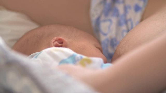 Close-up shot of newborn baby breastfeeding with following view to tired and sleepy mother who can hardly open eyes