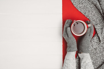 Female hand holding a cup of tea or coffee on white wooden table. Winter or christmas cosy background. Photograph taken from above, top view with copy space