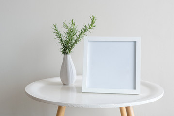Close up of sprigs of rosemary in small white vase with blank square frame on round table against...
