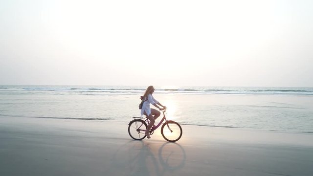 A young woman rides on the beach in a beautiful sunset. The camera moves from the girl beautiful flying red flag rescue. Aerial view.