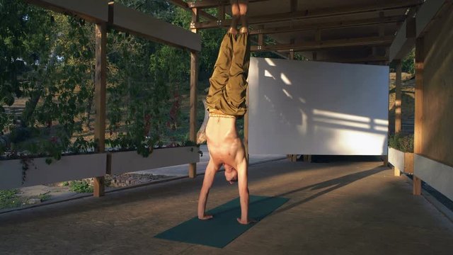 Young Yogi with a Naked Torso Performs a Rack on Hands on a Wooden Pomo Early in the Morning in the City Park