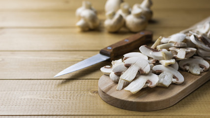 Fresh sliced mushrooms on chopping Board and onion and herbs on wooden table.
