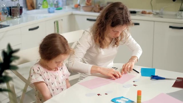 A woman with a girl doing an application of colored paper sitting at a table at home