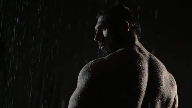 Powerful muscular man warrior stands in the rain with his back to the camera. he turns his head