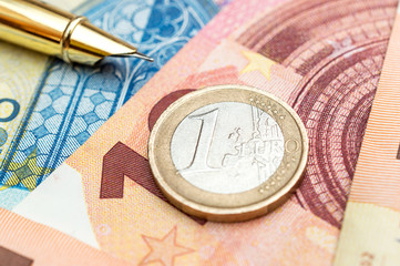 One euro coin with pen on euro bills. Close up. Business concept.