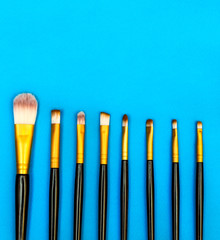 Row of makeup brushes on blue background. Top view.