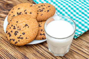 Glass of milk, cookies with chocolate and kitchen towel on the table.