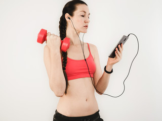 Stylish woman listening to music using a smartphone while exercising with dumbbells