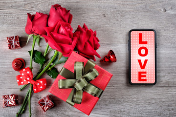 Happy Valentine's Day Concept with red roses, gift boxes, smartphone and love word on mobile screen