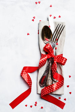 Festive table setting for Valentines Day, set of cutlery, red ribbon and sweet hearts, gray background, top view