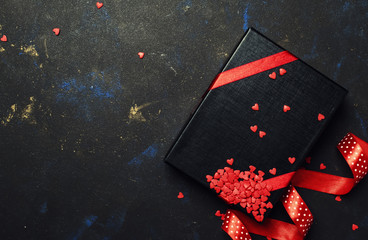 Gift for man on Valentines day, black box with red ribbon and sweet hearts, dark background, top view