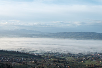 Beautiful view of Umbria valley in a winter morning, with fog covering trees and houses