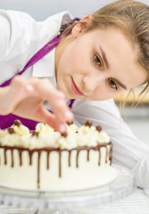 Young woman decorating chocolate cake in the kitchen