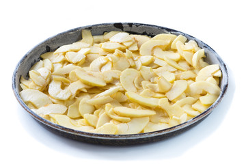 Phase of preparation of an apple pie. Baking tin with apples cut into thin slices on which the dough will be poured. White background